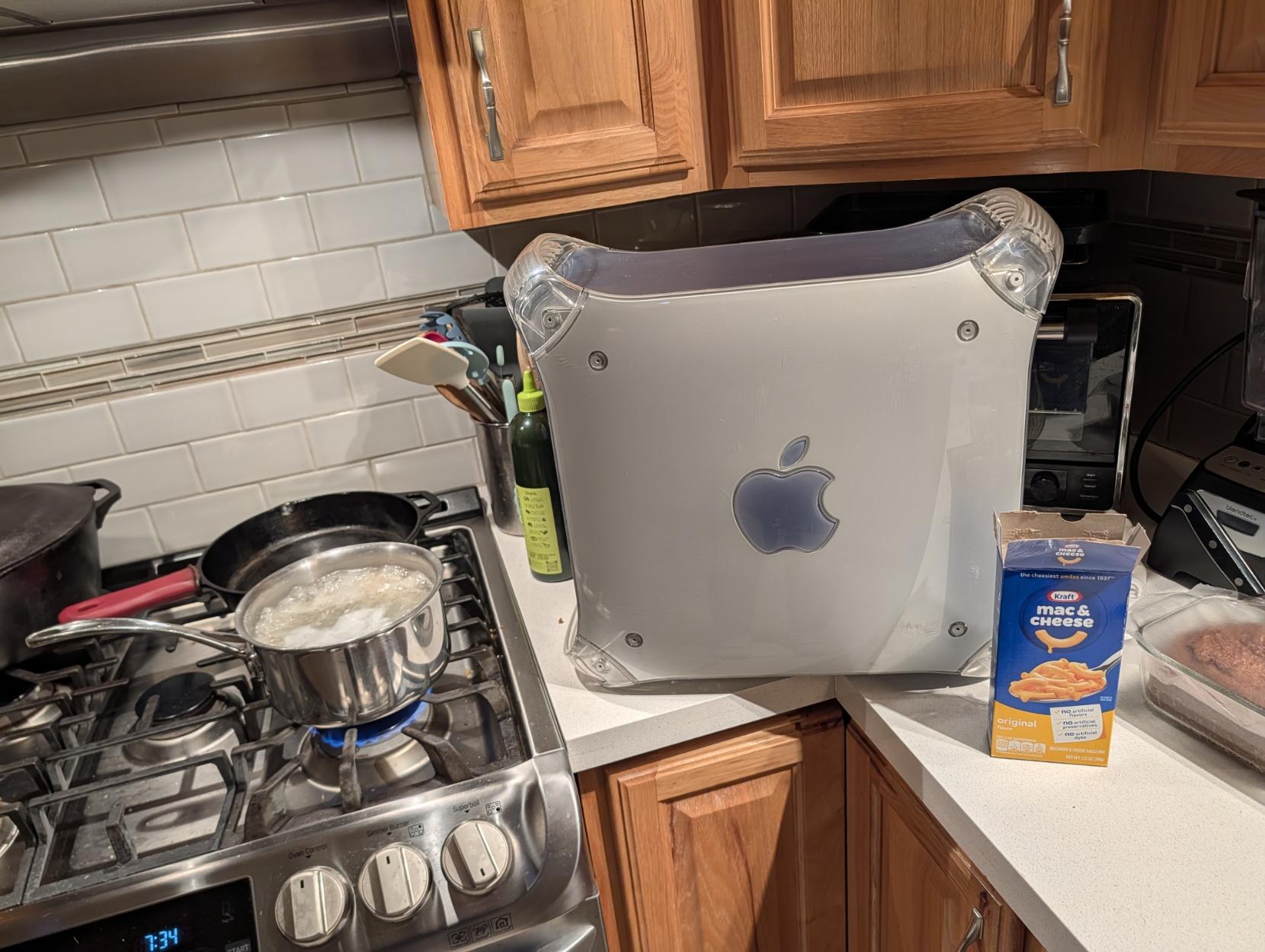 a powermac g4 sat next to an oven with a pot and a box of mac and cheese